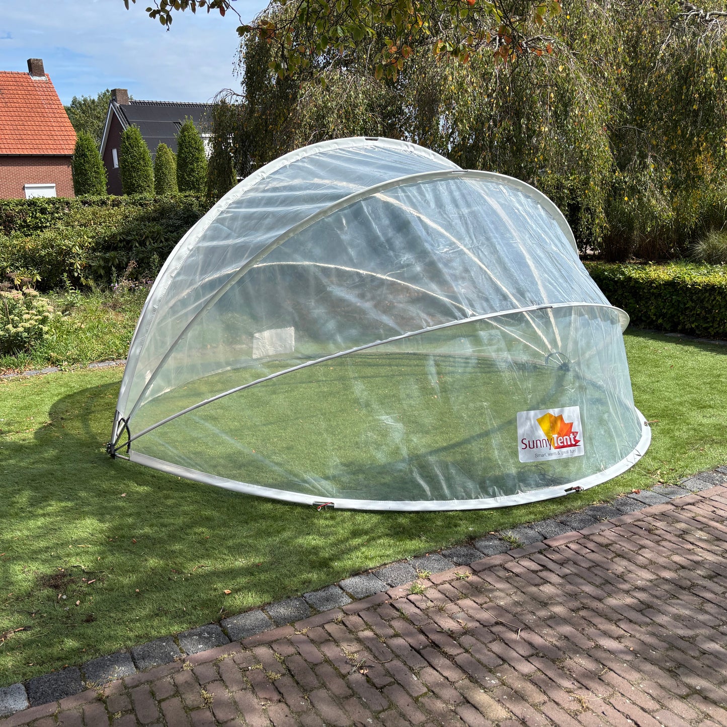 Clear plastic dome on a grassy area with a house and trees in the background